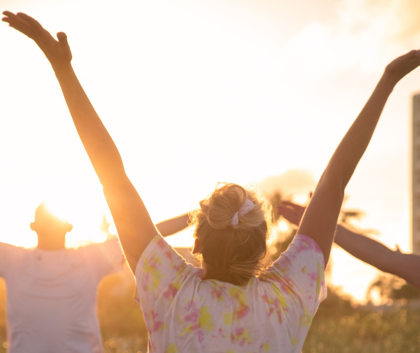 Friends raising their arms to the sun during beach yoga